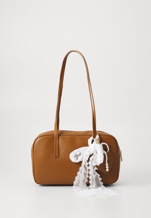 Bolso de cuero marrón con dos asas, decorado con un lazo de encaje blanco y un accesorio con perlas en el lado derecho.