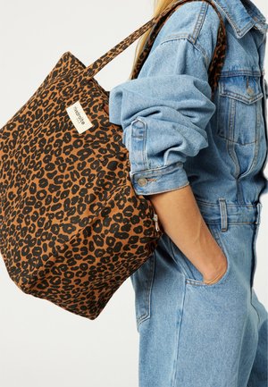 Brown leopard print canvas tote bag with a large, roomy design and two long handles, featuring a small label on the side.