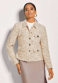 Crème tweedjas met een gestructureerde afwerking, voorzien van een kraag, voorkezen en knoopsluitingen. Gepaard met een satijnen rok.