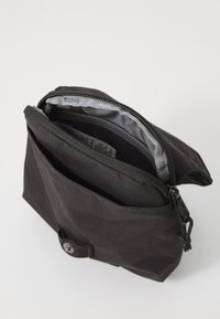 Fekete, strapabíró anyagból készült tasak, cipzárral záródik, elülső zsebbel rendelkezik, és a bélésének textúrája csíkos mintázatú.