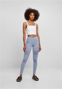 Hvit avkortet tanktop, lyseblå leggins med nettpaneler og svarte sandaler. Enkel design, tettsittende fasong og myk tekstur.