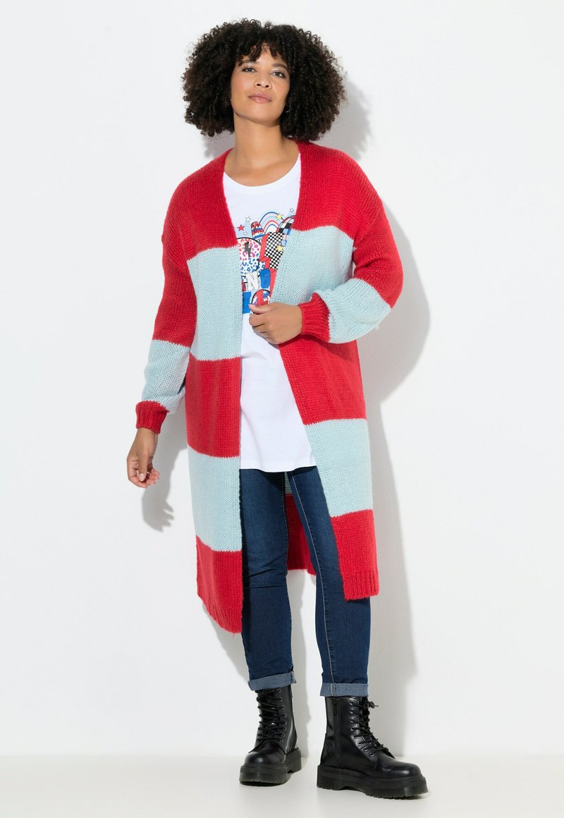 Roter und hellblauer gestrickter langer Cardigan mit offener Vorderseite, der Blockmuster, gerippte Bündchen und Seitenschlitze aufweist. Kombiniert mit einem weißen Grafik-T-Shirt und Jeans.