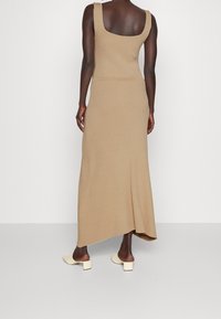 Beige geripptes Maxikleid mit tailliertem Oberteil, runder Rückenpartie und asymmetrischem Saum. Kombiniert mit hellen Blockabsatzschuhen.