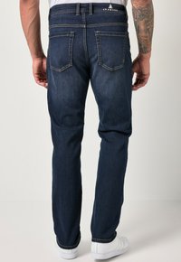 Jeans de mezclilla azul oscuro con diseño de pierna recta, cinco bolsillos, costuras amarillas en contraste y una cinturilla con marca en la parte trasera.