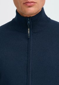Marinefarbener Reißverschluss-Pullover mit hohem Kragen, aus strukturiertem Strickstoff gefertigt, mit einem sichtbaren Reißverschluss und "SOLID"-Branding an der Zuglasche.
