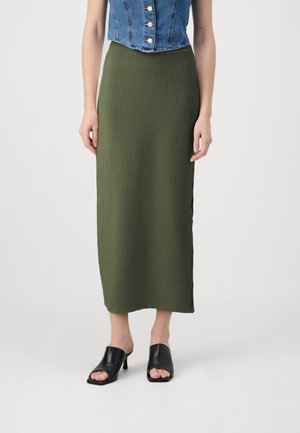 Grønn ribbet strikket midi-skjørt med en rett silhuett. Brukt med svarte åpne tå hælmules. Denimbekortet topp har knappe detaljer.