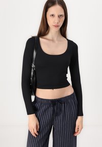 Must have pikkade varrukatega must crop-top ruudukujulise kaelusega, millele on lisatud siniste triipudega laiad püksid ja must õlakott. Sile kangas.