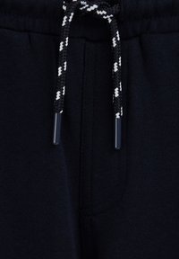 Schwarzer Stoff mit einer Nahaufnahme eines schwarz-weißen, geflochtenen Kordelzugs, der am Taillenbund eines Kleidungsstücks gebunden ist.