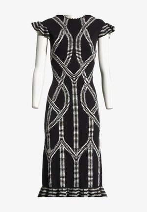 Robe noire cintrée avec des motifs géométriques blancs à pois, manches courtes volantées et ourlet à volants, exposée sur un mannequin blanc.