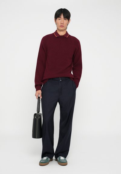 Maglione bordeaux con dettaglio del colletto arancione, pantaloni a righe blu navy, borsa nera, sneakers teal con lacci bianchi, vestibilità rilassata.