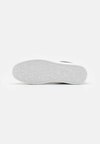 Semelle de sneaker blanche avec un motif géométrique de hexagones et de diamants, présentant une construction en caoutchouc épaisse et des rainures sur les côtés pour l'adhérence.