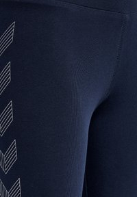 Navyblå leggings med en slät yta, med ett geometriskt vitt mönster på sidan. Designen innehåller skarpa linjer och vinklar.