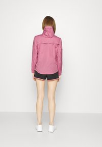 Lätt, rosa huva-jacka med en dragkedjeförsedd bakficka, paired med svarta shorts med rosa kant och vita sneakers.