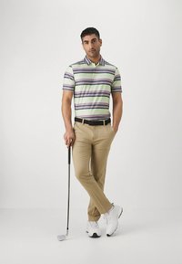 Polo às riscas com tons de verde, roxo e branco, combinado com calças caqui. Os acessórios incluem um cinto preto e um taco de golfe.