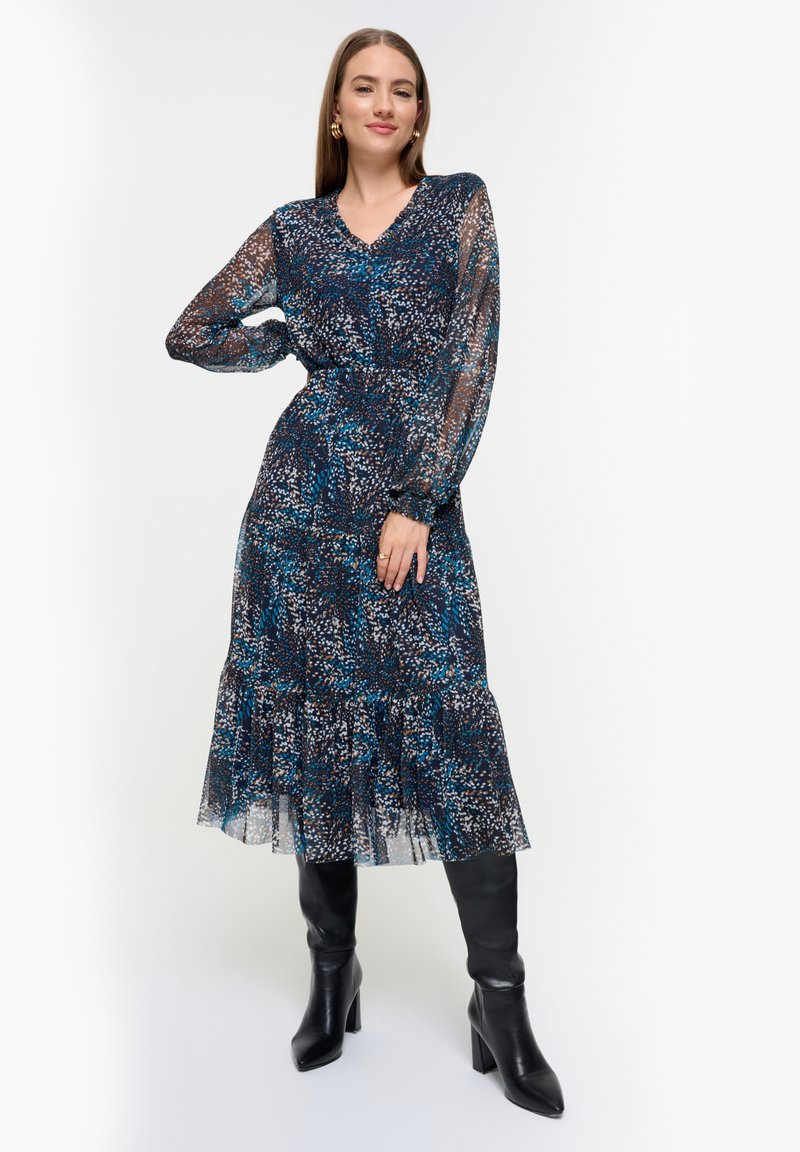 Bloemenpatroon, lange mouwen jurk in doorzichtige blauwe en zwarte stof, met een gathers taille en gelaagde rok. Gecombineerd met kniehoog zwarte laarzen.