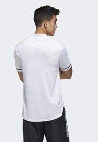 Hvid polo t-shirt med et subtilt strukturmønster, sorte stribede detaljer på ærmerne og et klassisk design. Bæres med sorte shorts.