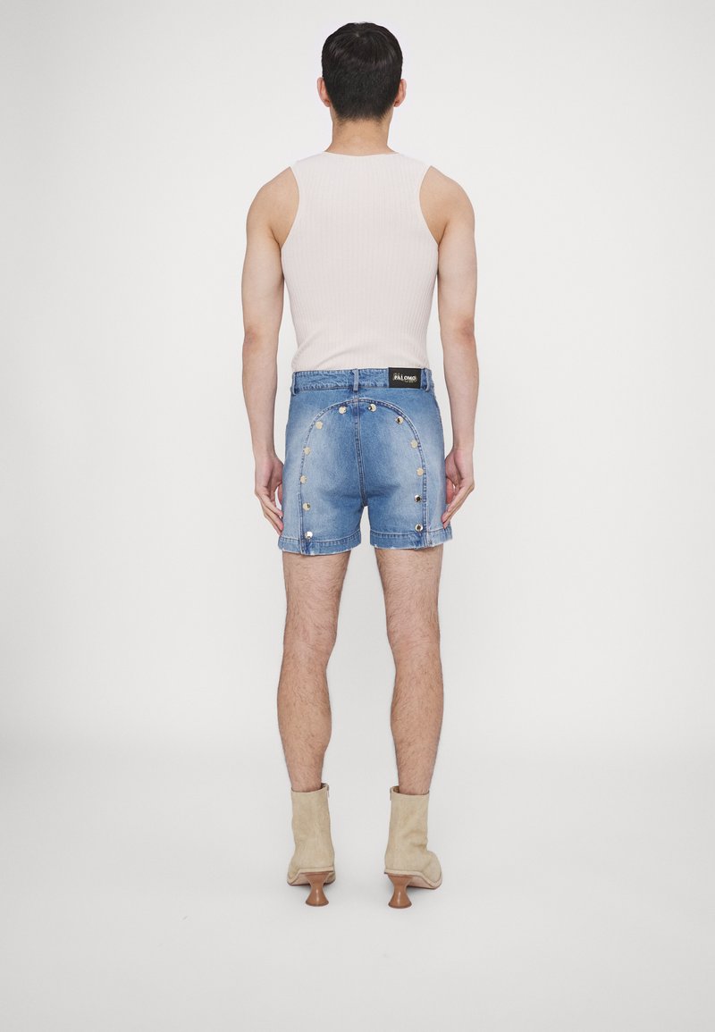 Shorts en denim au design ajusté, de couleur bleue, avec des accents en matériel rond uniques à l'arrière. Associés à une botte à talon beige.