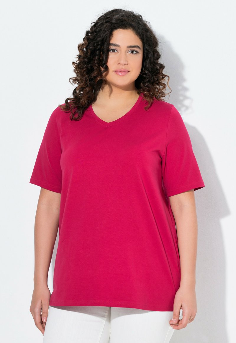 T-shirt fuchsia à col en V en coton doux, avec des manches courtes et une coupe décontractée, assorti à un pantalon blanc.