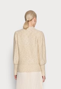 Cremfarbener Strickpullover mit puffigen Ärmeln und geripptem Saum. Die Textur weist dezente metallische Fünklchen für zusätzliche Details auf.