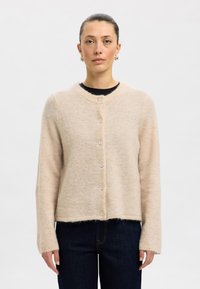 Ljusbeige stickad kofta i mjukt material, med rund halsringning, långa ärmar och sex knappar framtill. Casual passform med kortad fåll.