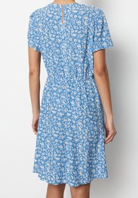 Blå blommig klänning med korta ärmar, elastiskt midjeband och öppen ryggdetalj. Tyget har vita blommönster överallt.