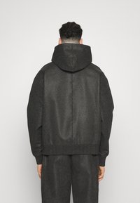 Chaqueta negra con capucha, de tejido texturizado, corte holgado y bajo de canalé. Presenta un diseño limpio y detalles minimalistas.