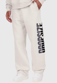 Gaišpelēki sporta bikses ar brīvu piegriezumu, kuras rotā melns teksturēts "DROPSIZE" prints pa kreiso kāju. Izgatavotas no mīksta kokvilnas materiāla.