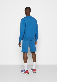 Sweatshirt bleu et shorts assortis en tissu doux, présentant un design simple et une coupe décontractée. Baskets avec des accents rouges et bleus.