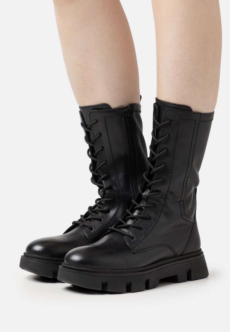 Botas de combate de cuero negro con cordones en la parte delantera, cremallera lateral y suela de goma gruesa, con costuras texturizadas a lo largo de la superficie.
