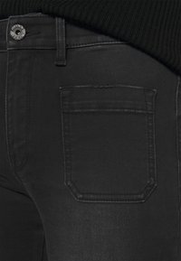 Los jeans de mezclilla negra presentan un bolsillo trasero de forma rectangular y costuras limpias, que destacan una textura suave y un brillo sutil.