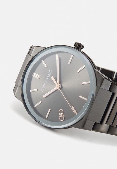 Men's wristwatch with a matte dark grey stainless steel case, minimalist grey dial, and silver hands. Features a sleek metal bracelet and logo.