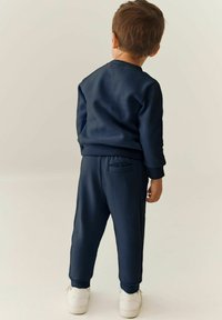 Navyblaues Sweatshirt- und Hosen-Set aus weichem, glattem Stoff. Die Hose verfügt über Seitentaschen; das Sweatshirt hat gerippte Bündchen und Saum. Getragen mit weißen Sneakern.