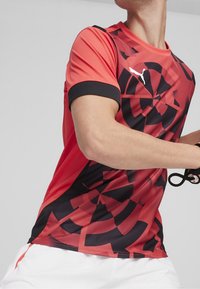 Czerwona i czarna koszulka sportowa z abstrakcyjnymi wzorami geometrycznymi, krótkim rękawem i okrągłym dekoltem. Wykonana z oddychaj�ącego materiału z detalem logo.