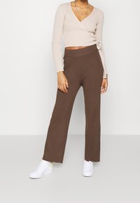 Beżowa, prążkowana bluzka z długim rękawem, zestawiona z brązowymi, prążkowanymi spodniami o szerokich nogawkach. Buty to białe trampki z żółtymi akcentami.