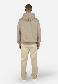 Beżowa bluza z kapturem, opadającymi ramionami i prążkowanymi mankietami; zestawiona z jasnobeżowymi szerokimi spodniami o miękkiej fakturze.