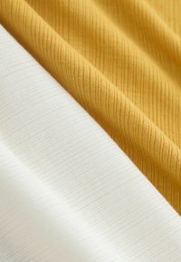 Gros plan sur un tissu côtelé plié de couleur jaune moutarde et blanc, montrant la texture et de fines lignes verticales.