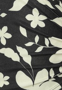 Tela negra con una textura brillante que presenta grandes patrones de flores y hojas blancas, creando un contraste y un interés visual.