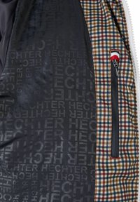 Binnenvoering van de jas met herhaalde "HECHTER" tekst op zwarte stof naast geruite stof met een verticale ritszak.