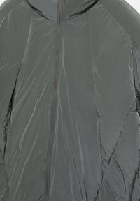 Veste légère à capuche de couleur gris foncé. Présente une texture froissée et une fermeture éclair frontale sur toute la longueur. Lignes épurées avec un minimum de détails.