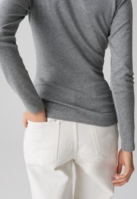 Maglietta a maniche lunghe grigia aderente, con una texture morbida, abbinata a jeans bianchi a vita alta con tasche applicate. Schema di colori neutri, look casual.