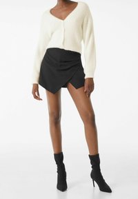 Vit fluffig kofta med V-ringning och långa ärmar, kombinerad med en svart omlott mini kjol och svarta klackade ankelskor.