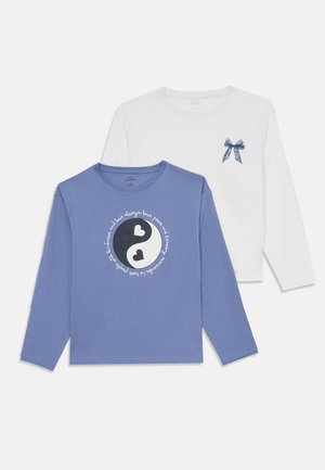 Camicie a maniche lunghe, una bianca con un fiocco blu sul petto, l'altra blu con un design yin-yang in bianco e nero e un cuore circondato da testo corsivo.