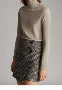 Maglione a collo alto grigio chiaro abbinato a una gonna a portafoglio scozzese scura con tre bottoni neri e una finitura testurizzata.