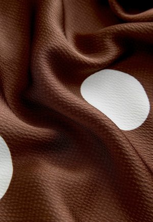 Brązowa tkanina o fakturze i gładkim układzie z białymi kropkami. Tkanina delikatnie się błyszczy i ma miękki, zachęcający wygląd.