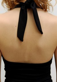 Zwarte haltertop met een strik om de hals. Glad materiaal, strak aansluitend design en minimalistische stijl. Blootgestelde huid op de rug.