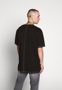 Svart t-skjorte med korte ermer, med kontrastfarget grønn søm og en avslappet passform. Grå jeans med en teksturert finish.