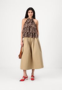 Top cu guler halter, cu imprimeu leopard și design volă; fustă plisată bej; saboți cu toc roșii, cu vârful ascuțit; geantă maro cu curea.