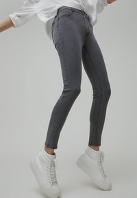 Jeans ajustados de tiro alto en gris, confeccionados en denim elástico, que presentan bolsillos delanteros y costuras en contraste. Combinados con zapatillas altas blancas.