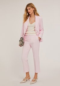 Roze op maat gemaakte blazer en bijpassende cropped broek, gecombineerd met een crèmekleurige gebreide top en een slangenprint clutch. Puntige beige hakken met banddetail.