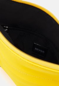 Sacchetto giallo con zip aperto per mostrare l'interno nero con una piccola tasca con zip e un'etichetta cucita BOSS Hugo Boss.
